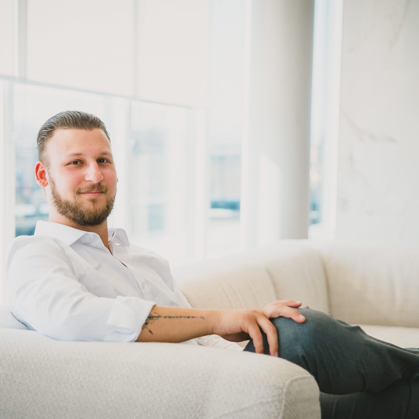 Photo of Arnold Gluck, Century 21 United REALTOR and your local REALTOR sitting on a cream couch looking at the camera.